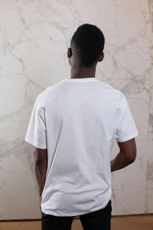 a man standing in front of a white wall, back view. nuri iyem, white t-shirt, background image, multiple stories