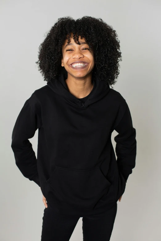 a woman in a black hoodie standing with her hands on her hips, a portrait, trending on unsplash, dark short curly hair smiling, black teenage boy, blank background, no - text no - logo