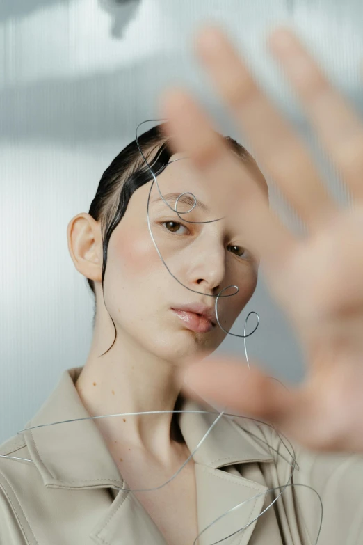 a woman holding her hand up in front of her face, an album cover, inspired by Anna Füssli, trending on pexels, hyperrealism, bright thin wires, japanese model, shaven face, issey miyake
