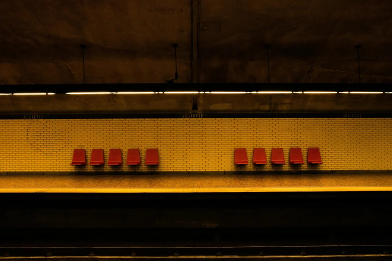 a row of red chairs sitting on top of a train platform, inspired by Andreas Gursky, unsplash contest winner, yellow light, ignant, in a subway, brown