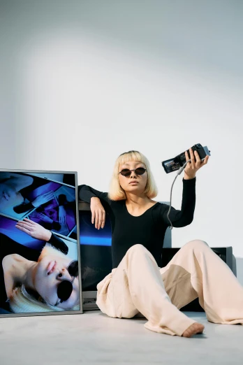 a woman sitting on the ground holding a camera, an album cover, inspired by Wang E, video art, technological sunglasses, watching tv, long boi, shot with sony alpha