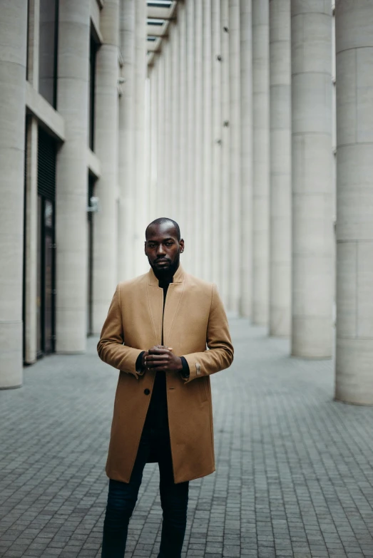 a man standing in the middle of a walkway, an album cover, inspired by Theo Constanté, pexels contest winner, light brown coat, yasuke 5 0 0 px models, mc ride, elegant pose
