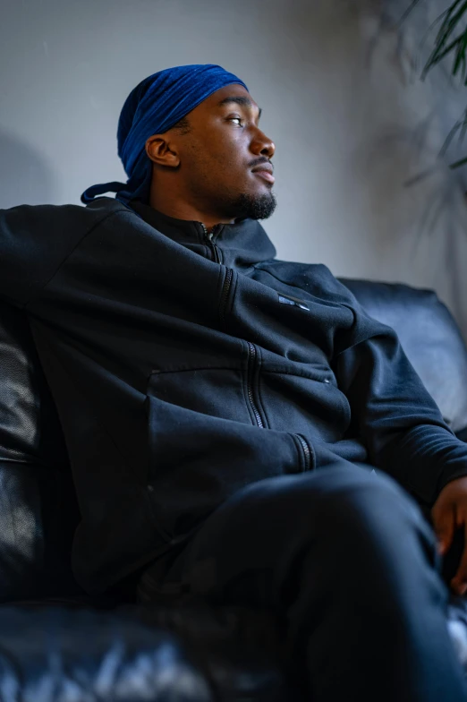 a man sitting on a couch in a living room, wearing a black hoodie, yzy gap, profile image, wearing a plug suit