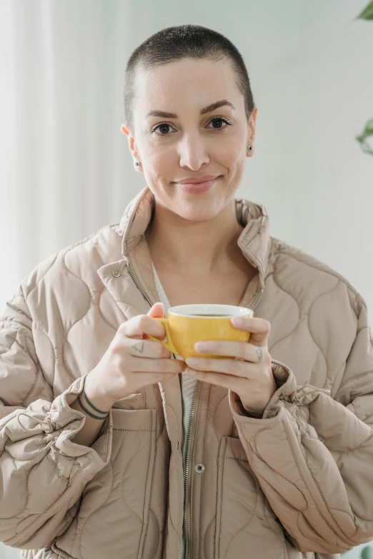 a woman holding a cup of coffee in her hands, a portrait, trending on pexels, wearing a yellow hoodie, model wears a puffer jacket, mid - 3 0 s aged, angelina stroganova