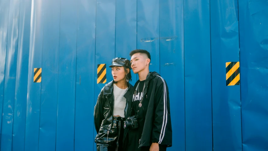 a man and a woman standing in front of a blue wall, unsplash, graffiti, she wears leather jacket, asian, wearing a track suit, avatar image