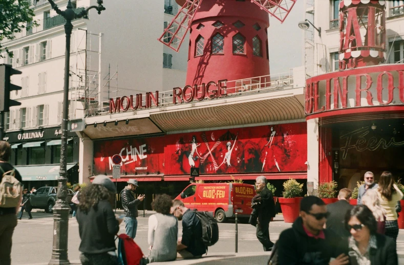 a group of people standing in front of a red building, moulin rouge, it has a red and black paint