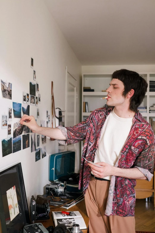 a man standing in front of a wall with pictures on it, trending on pexels, declan mckenna, in a japanese apartment, engineer, painting