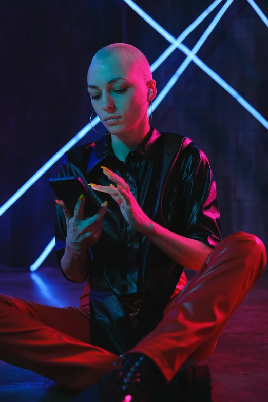 a woman sitting on the ground using a cell phone, antipodeans, shaved bald head, cyber neon lighting, dramatic reading spell book pose, neon jungle