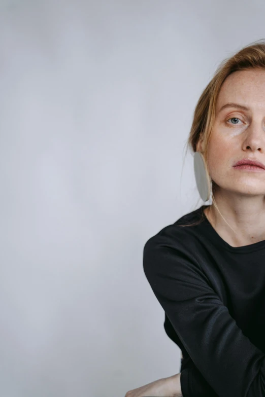 a woman sitting on a chair in front of a white wall, a character portrait, trending on unsplash, realism, prominent jawline, olya bossak, wearing a black sweater, concerned expression