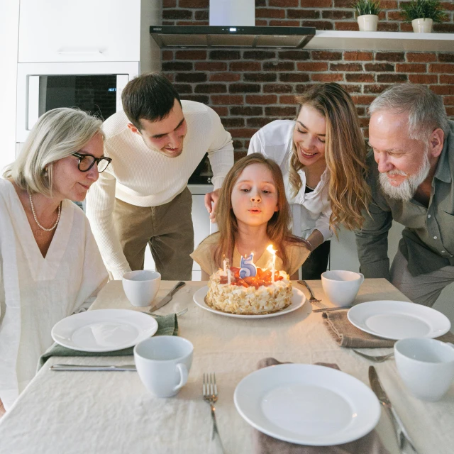 a group of people standing around a table with a cake, by Carey Morris, pexels, perfect android girl family, old man, on a candle holder, birthday cake on the ground