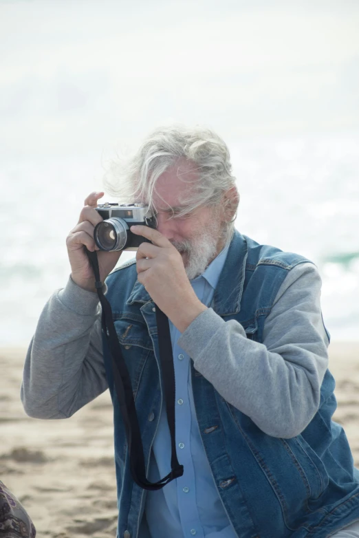 a man taking a picture with a camera on the beach, by Peter Churcher, photorealism, gray hair and beard, medium format, 15081959 21121991 01012000 4k, action photograph