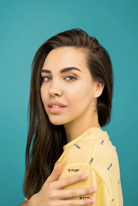 a woman with long brown hair wearing a yellow shirt, a colorized photo, inspired by Elsa Bleda, trending on pexels, photorealism, teal studio backdrop, :: madison beer, aubrey plaza, androgynous person