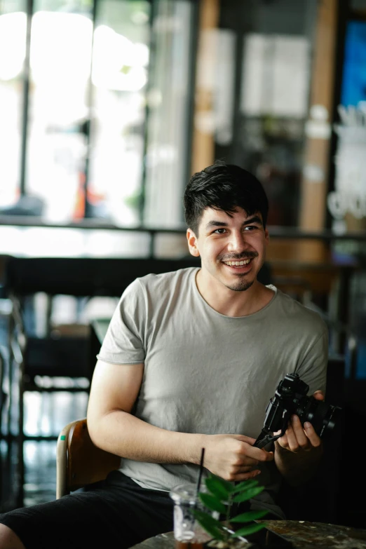 a man sitting at a table holding a camera, smiling for the camera, mark edward fischbach, headshot profile picture, aykut aydogdu zener