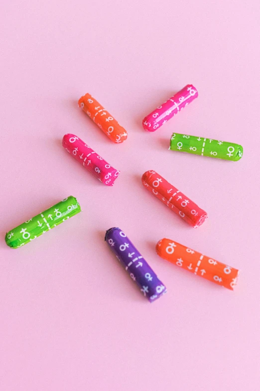 a pile of colorful erases sitting on top of a pink surface, simple primitive tube shape, rune marks, made of lollypops, detailed product image