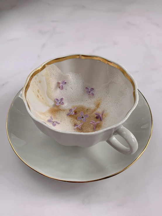 a close up of a cup and saucer on a table, inspired by Maud Naftel, process art, gold flaked flowers, lilac, cappuccino, real porcelain texture effect