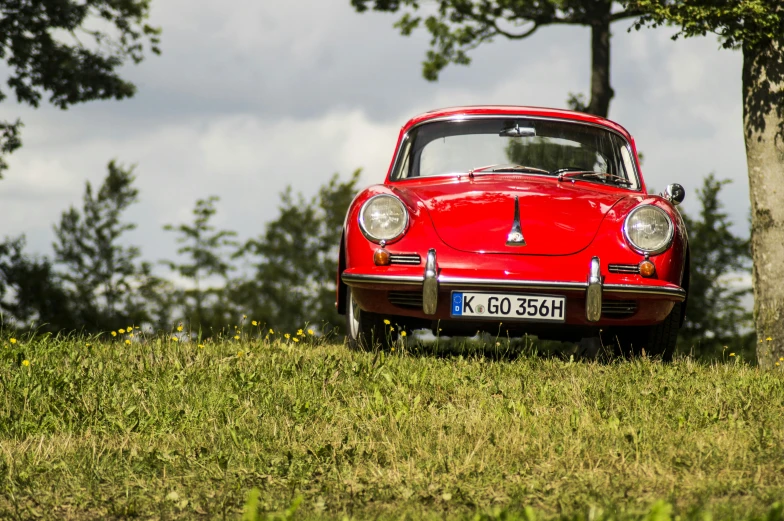 a red car sitting on top of a lush green field, by Matthias Weischer, pexels contest winner, 1974 porsche 911, retro style ”, front on, 15081959 21121991 01012000 4k