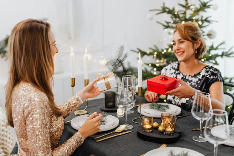 two women sitting at a table in front of a christmas tree, pexels contest winner, giving gifts to people, gentlemens dinner, on a white table, black