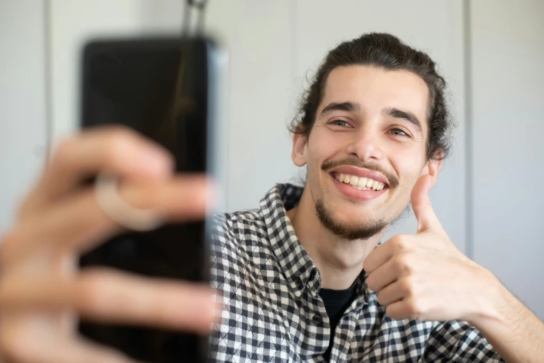 a close up of a person holding a cell phone, pexels contest winner, photorealism, goofy smile, young spanish man, doing a thumb up, discord profile picture