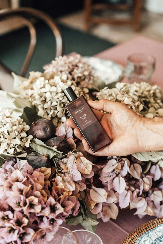 a person holding a cell phone next to a bunch of flowers, antique perfume, muted brown, harvest, hydrangea