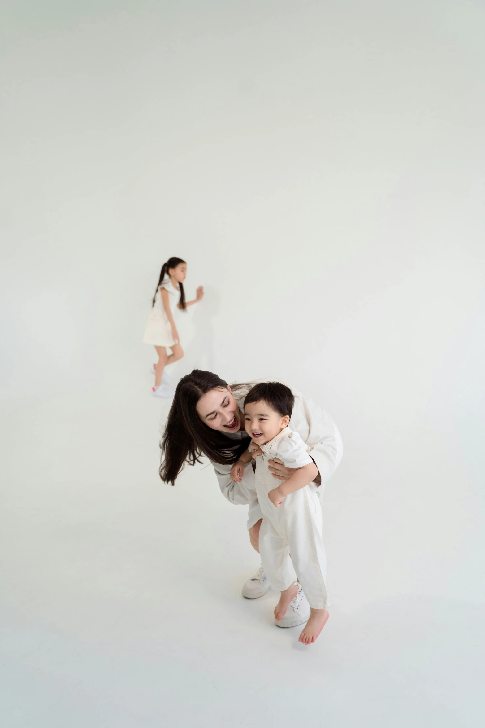 a woman standing next to a child in a white room, inspired by Li Di, pexels contest winner, playful pose, portrait of family of three, in front of white back drop, nanae kawahara