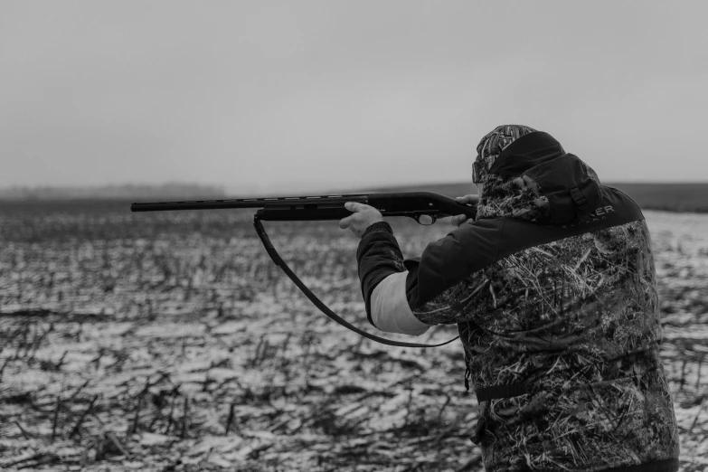 a man holding a rifle in a snowy field, a black and white photo, by Matt Cavotta, pexels, farming, game ready, shotgun, fall season