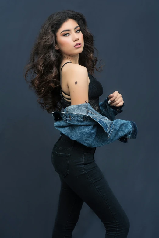 a woman in black pants and a denim jacket, an album cover, by Natasha Tan, trending on pexels, curly dark hair, tattoo, at a fashion shoot, actress