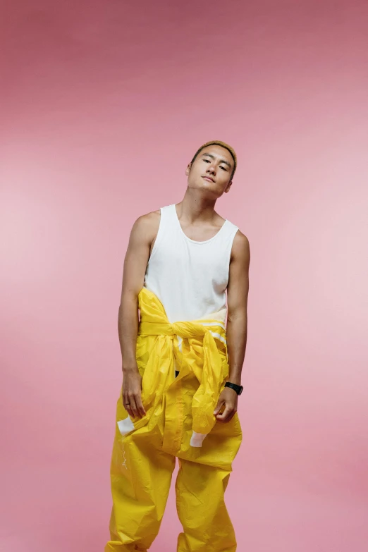 a man standing in front of a pink background, an album cover, inspired by Russell Dongjun Lu, happening, yellow clothes, joel fletcher, wearing a low cut tanktop, glossy from rain