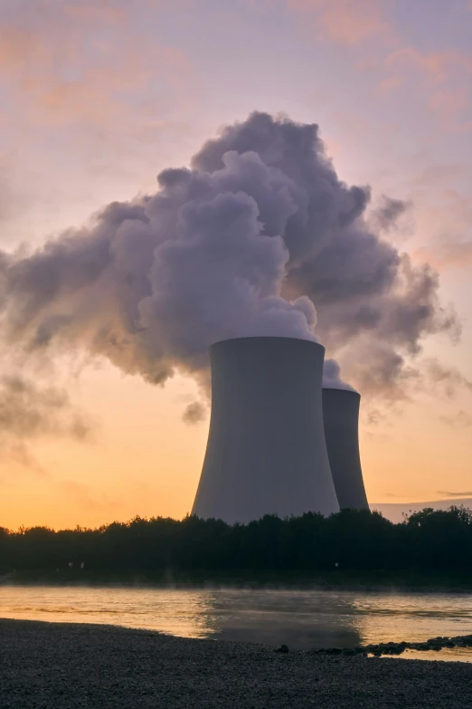 a couple of cooling towers next to a body of water, a picture, unsplash, nuclear art, crepuscule, 2022 photograph, historical image, icbm