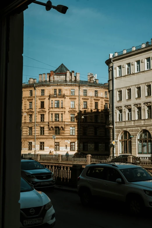 a group of cars driving down a street next to tall buildings, inspired by Vasily Surikov, pexels contest winner, neoclassicism, sunny bay window, view from back, saint petersburg, inside an old apartment