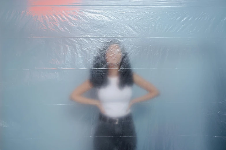 a woman standing in front of a wall covered in plastic, an album cover, inspired by Elsa Bleda, pexels contest winner, on a pale background, plastic wrap, blurry photo, woman with black hair