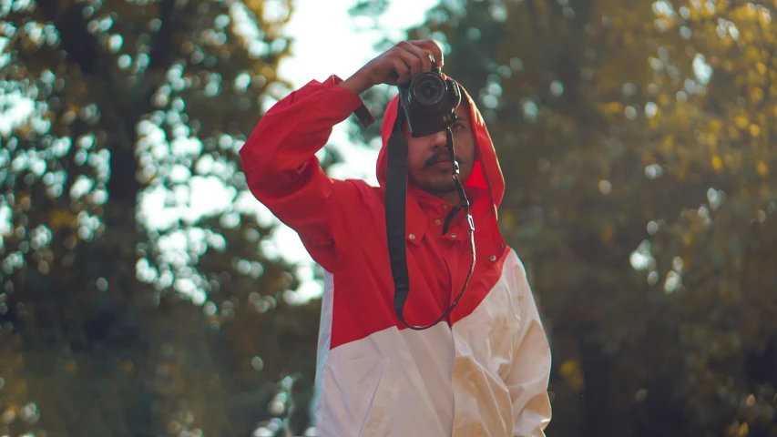 a man taking a picture with a camera, by Attila Meszlenyi, visual art, red hoodie, wearing a track suit, drenched clothing, outdoor photo