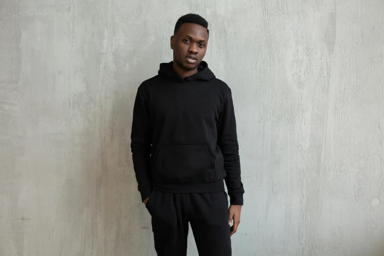 a man standing in front of a concrete wall, black hoodie, wearing a hoodie and sweatpants, or black, front