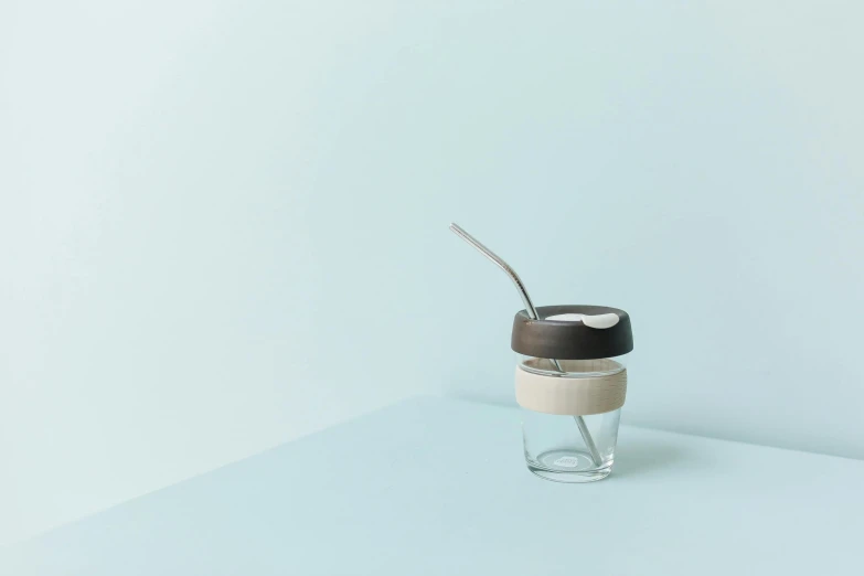 a cup with a spoon in it sitting on a table, unsplash, minimalism, glass jar, silicone skin, brown, light grey