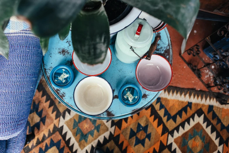 a person standing next to a table with cups on it, inspired by Wes Anderson, trending on unsplash, cloisonnism, outdoors mesa setting, high angle close up shot, blue colour scheme, at home