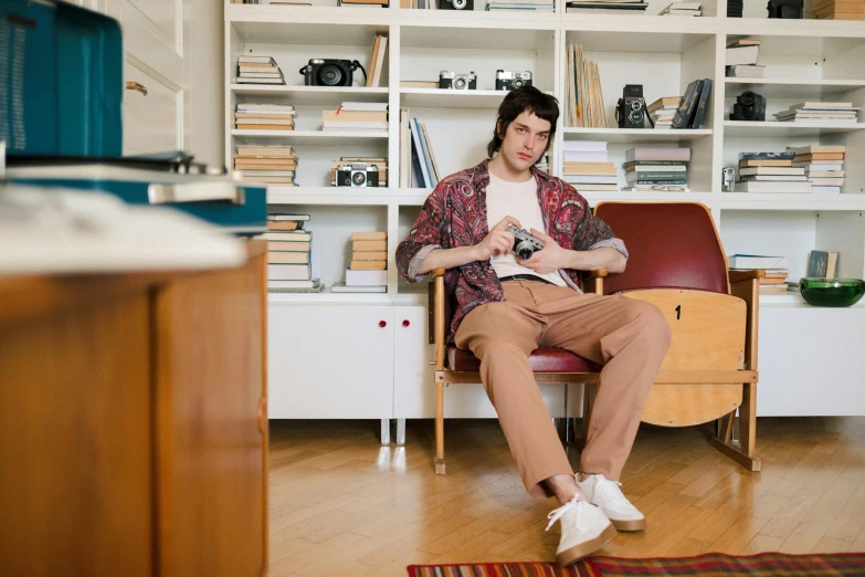 a man sitting in a chair reading a book, an album cover, pexels contest winner, brown pants, young handsome pale roma, apartment, in the style wes anderson