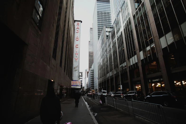 a group of people walking down a street next to tall buildings, broadway, background image, vsco, [ theatrical ]