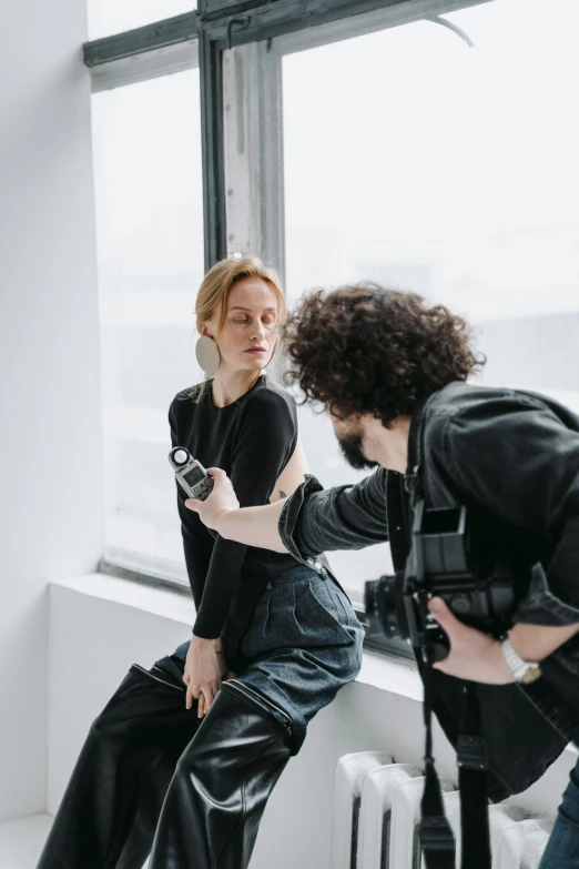 a man taking a picture of a woman sitting on a window sill, by Nina Hamnett, trending on pexels, in a studio, wearing a designer top, model is wearing techtical vest, expert artist