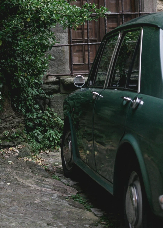 a green car parked on a cobblestone street, inspired by Elsa Bleda, pexels contest winner, renaissance, grainy movie still, hillside, moskvich, close-up shot taken from behind