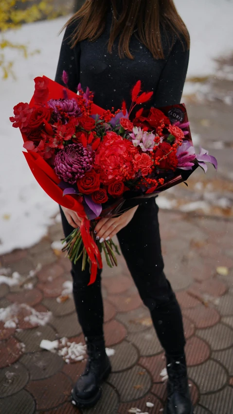 a woman standing in the snow holding a bunch of flowers, by Julia Pishtar, black and red color scheme, purple and red flowers, full product shot, a cozy