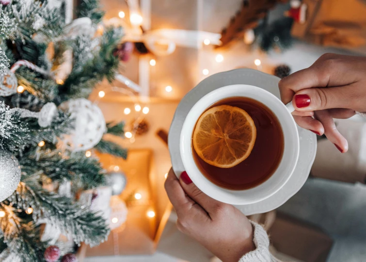 a woman holding a cup of tea in front of a christmas tree, a photo, by Julia Pishtar, trending on pexels, hurufiyya, lemon, gourmet and crafts, thumbnail, decoration around the room