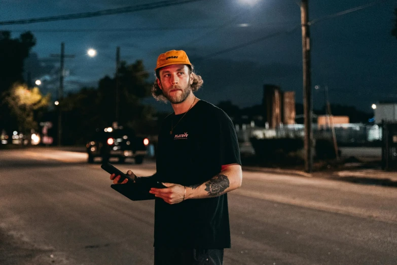 a man standing on a street holding a skateboard, unsplash contest winner, glowing visor, post malone, with orange street lights, heath clifford