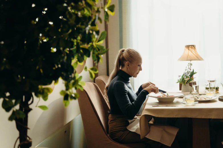 a woman sitting at a table with a plate of food, profile image, cozy environment, premium quality, carefully crafted