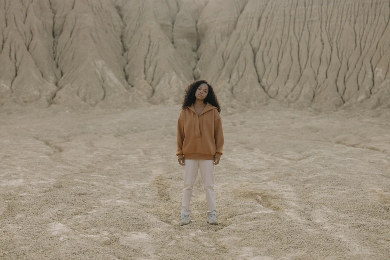 a woman standing in the middle of a desert, an album cover, pexels contest winner, wearing a hoodie and sweatpants, brown skin like soil, ☁🌪🌙👩🏾, full body within frame