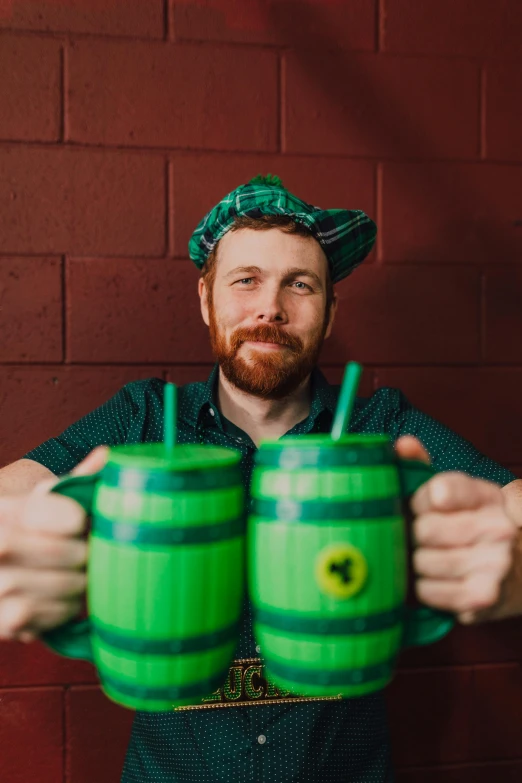 a man holding two green cups in front of a brick wall, a portrait, reddit, octoberfest, red beard, 15081959 21121991 01012000 4k, lachlan bailey