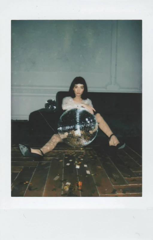 a woman sitting on the floor with a disco ball, a polaroid photo, hailee steinfeld, digital image, scanned, lily frank