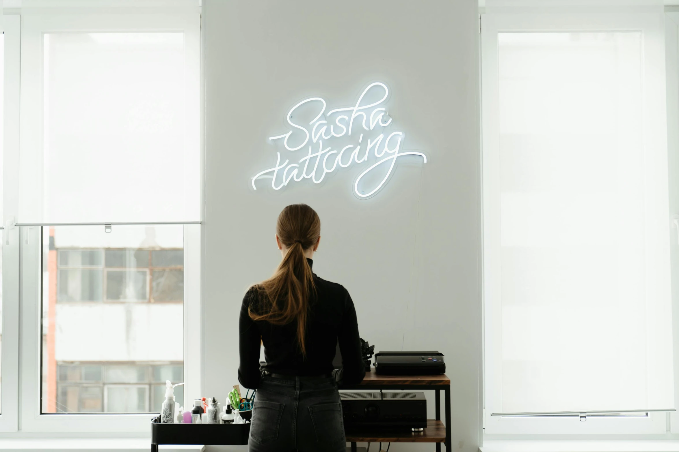 a woman standing in front of a wall with a neon sign, a tattoo, by Sebastian Spreng, trending on unsplash, on a white table, sat in an office, above lighting, caligraphy