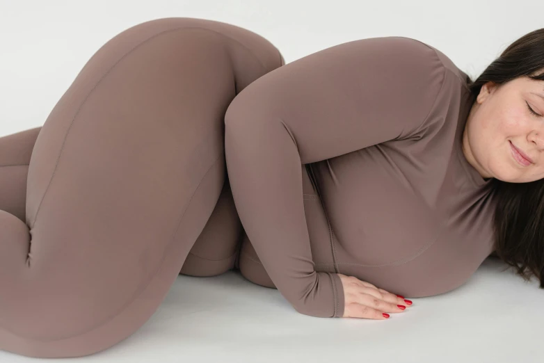 a woman laying on her stomach with her eyes closed, inspired by Sarah Lucas, leggings, taupe, smooth curvature design, chocolate