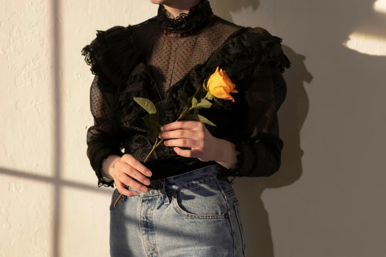 a woman standing in front of a wall holding a rose, inspired by Elsa Bleda, pexels contest winner, renaissance, black and yellow, mesh shirt, victorian lace, wearing denim