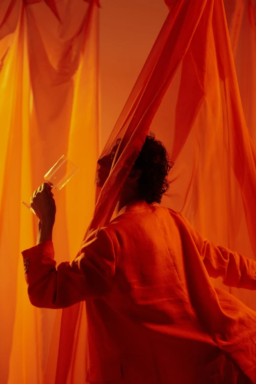a man in a red robe holding a pair of scissors, inspired by Christo, gutai group, colors orange, ethereal curtain, movie filmstill, orange