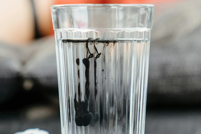 a glass of water sitting on top of a table, inspired by Lucio Fontana, unsplash, photorealism, full of tar, licorice allsort filling, close-up product photo, al fresco
